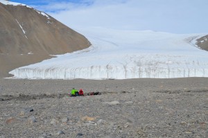 Joseph Levy and Jackie Watters collect soil measurements from within a water track (zone of enhanced soil moisture) in Taylor Valley. These measurements will help characterize the geologic controls on the existence and location of shallow groundwater in Antarctica's Dry Valleys, important for determining which areas of the valleys are stable. Howard Glacier is seen in the background. (Photo by Logan Schmidt)