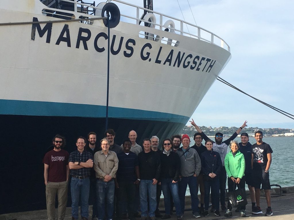 The group posing at the dock with the the prow of the Marcus Langseth looming over them.