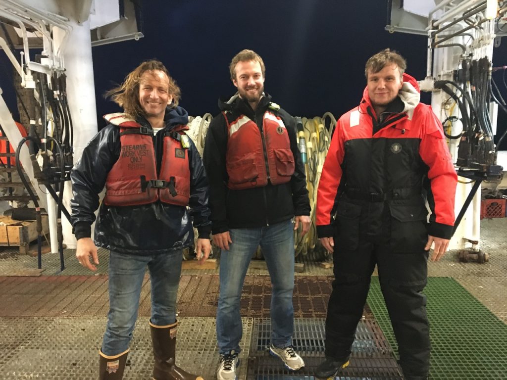 Three people in life vest posing for the camera at night on a science vessel.