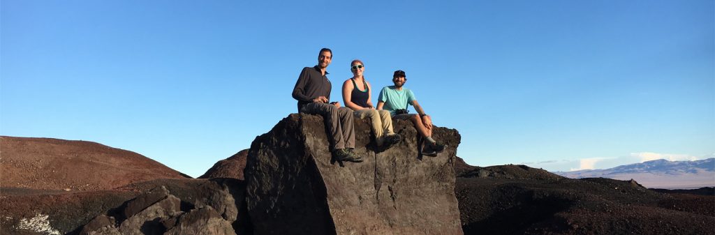 Photo of three people sitting on rock.