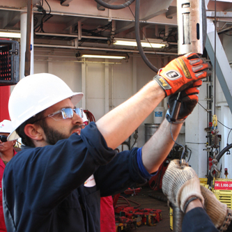 Researcher wearing a hard hat and gloves on a rig floor.