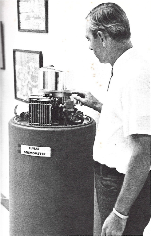 old black and white photo of a man next to an object on a column labelled lunar seismometer