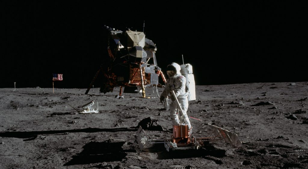 Photo of an Apollo 11 astronaut on the surface of the moon, with the lunar module behind him.