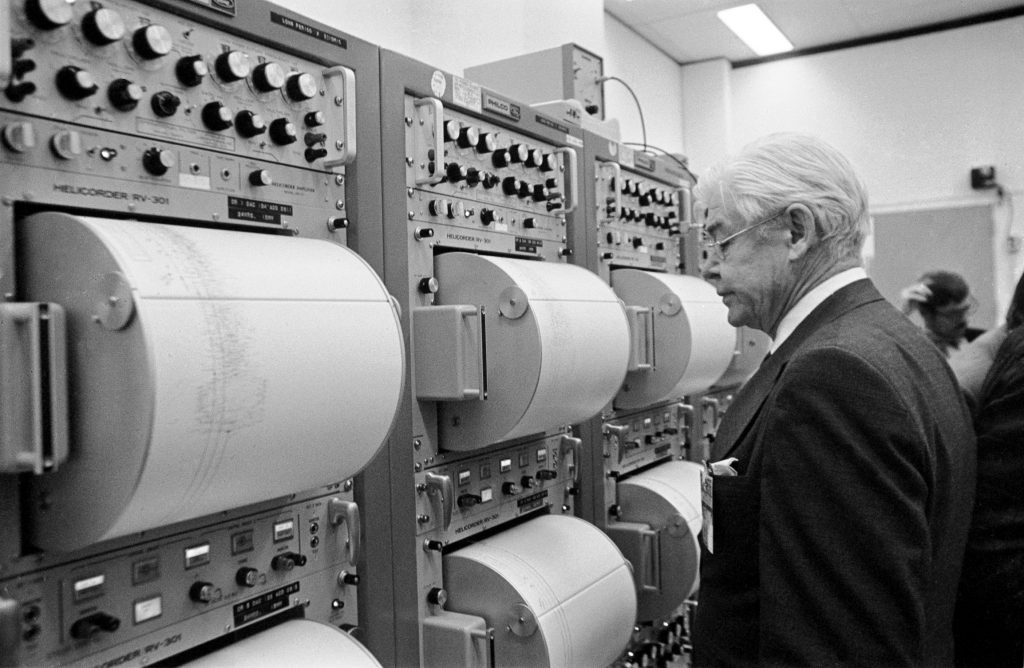 Black and white of Prof. Ewing examining tall computer banks and seismographs. 