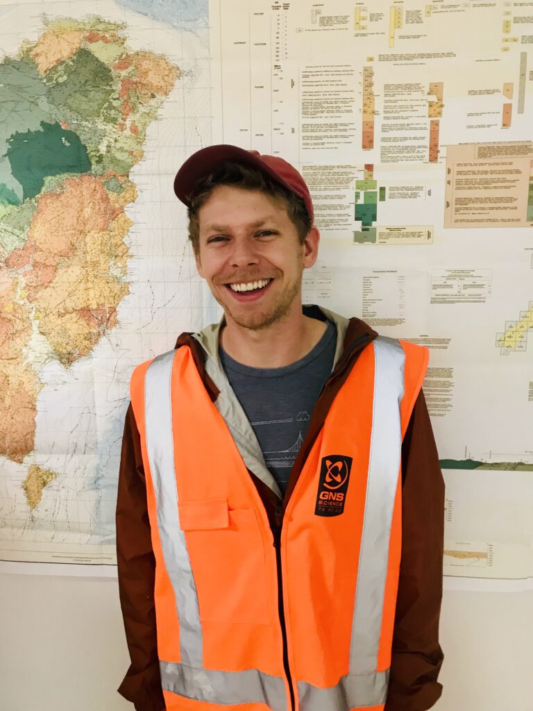 Portrait of Andrew Gase wearing a high-vis jacket stadning in front of a map or chart