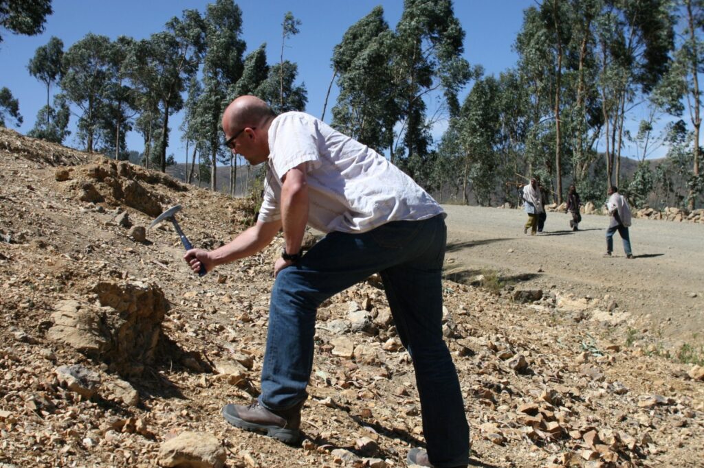 Field photo showing Thorsten Becker hitting a rock with a hammer.