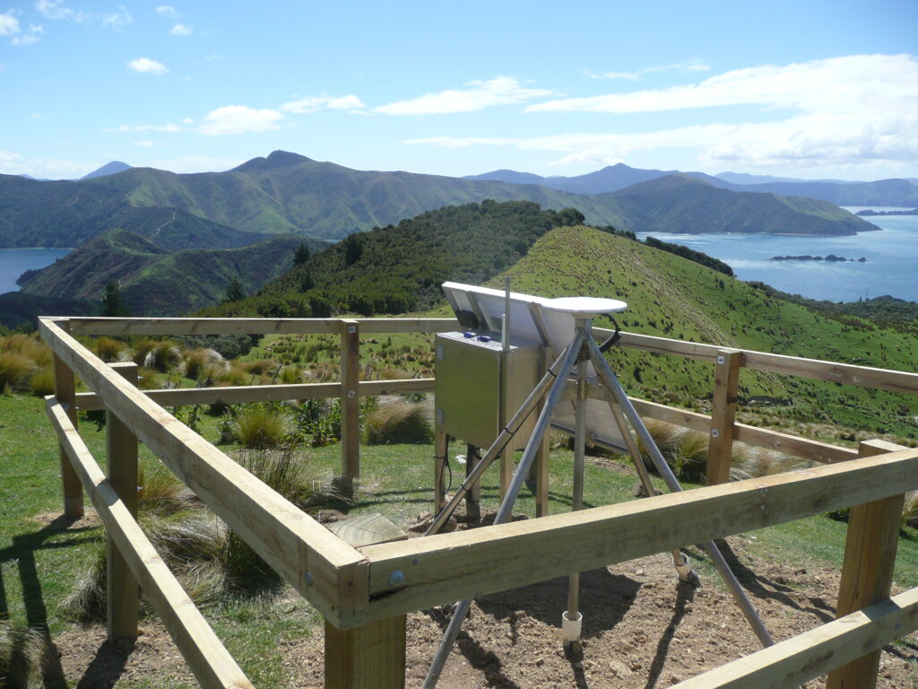 A GPS station on a hilltop overlooking mountains and water.