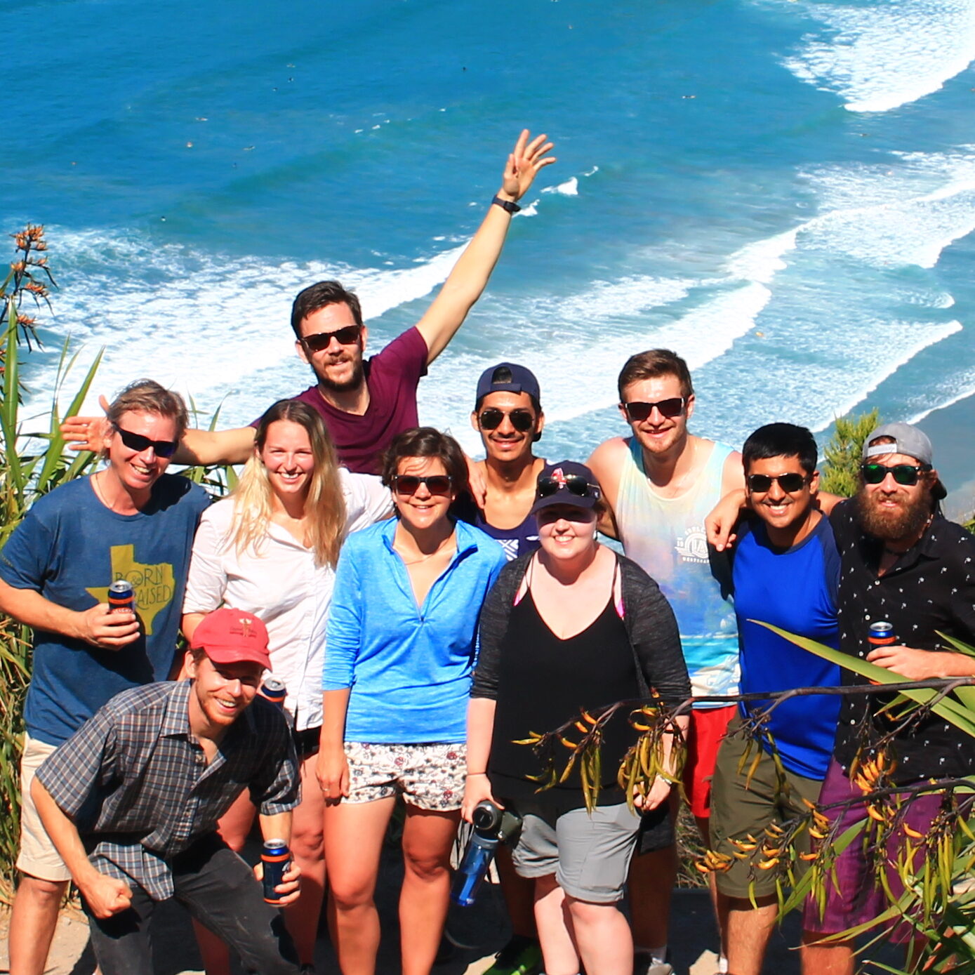 a group of students waves at the camera in front of a tropical beach landscape