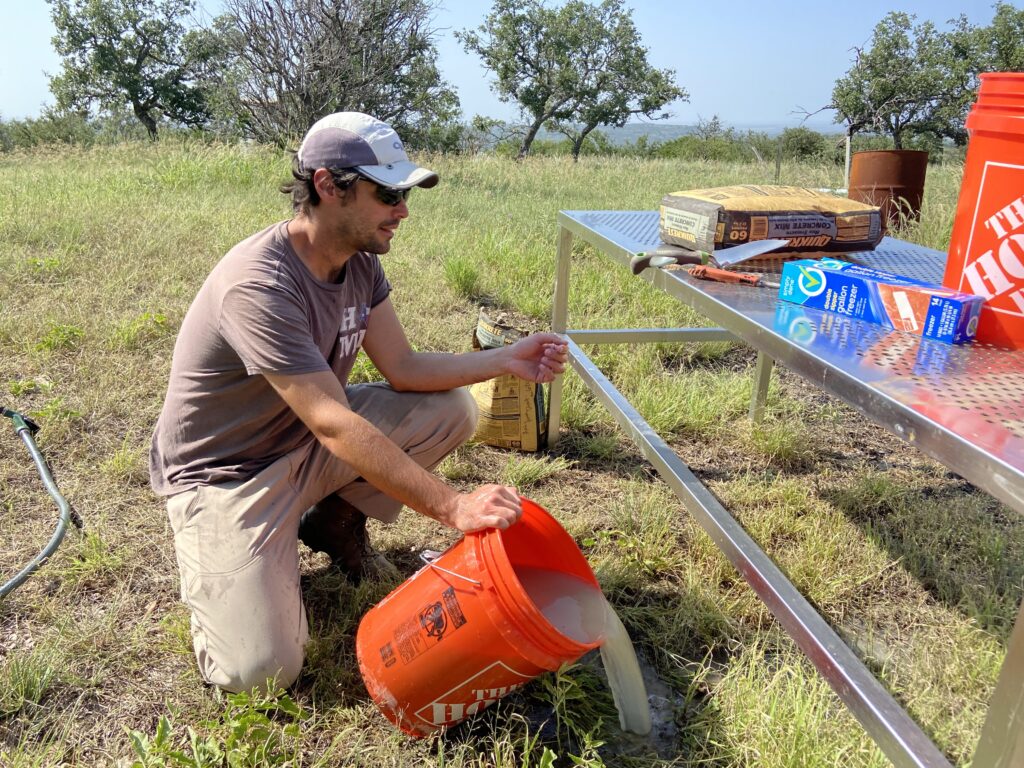 Zach in a field emptying an orange buck of sandy water.
