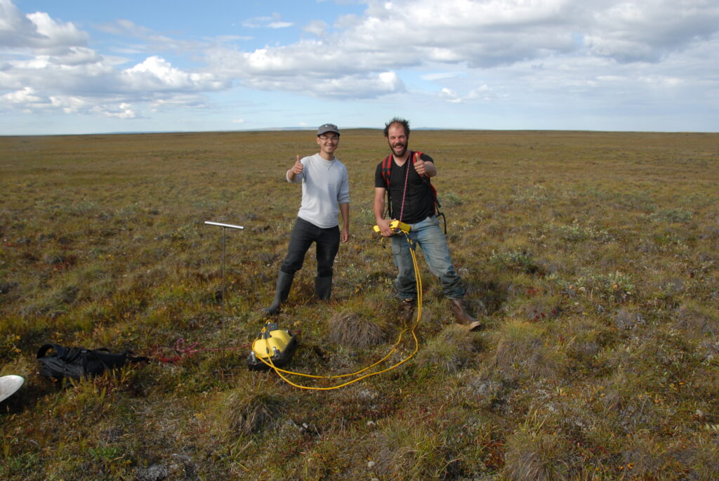 Two scientists in a grassy field pose for the camera.