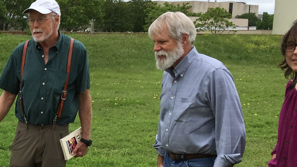 Photo of Mark outdoors. Larry Lawver is standing to one side. They are both looking at something off camera