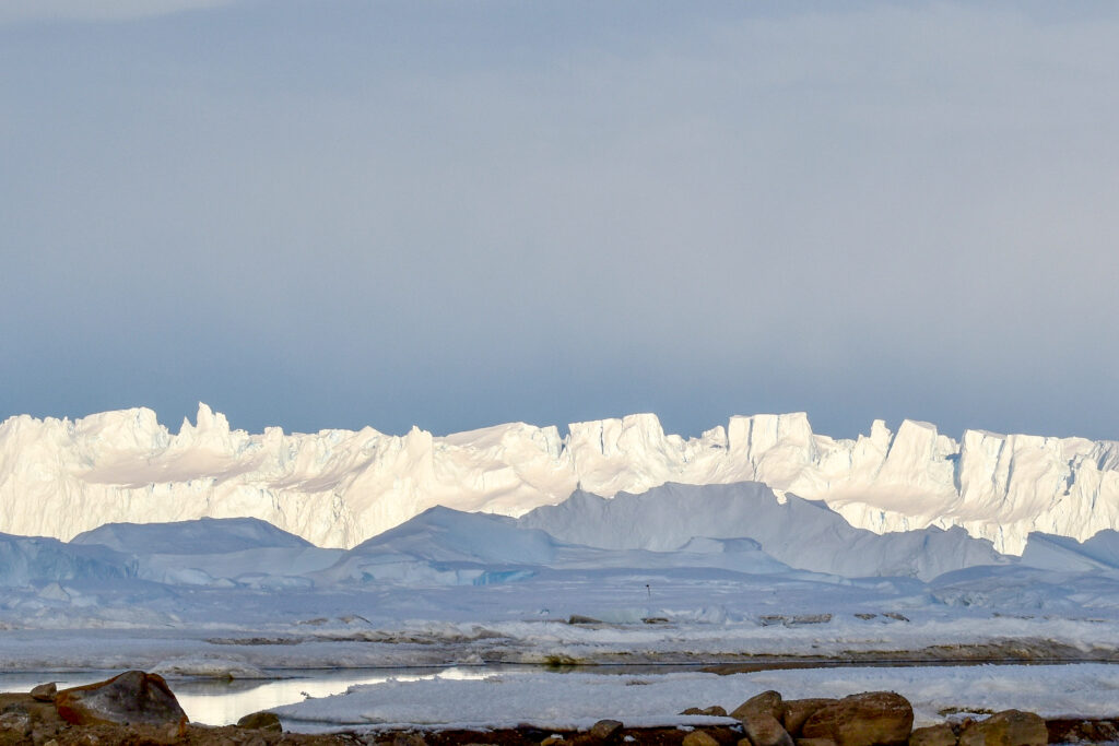 A wall of ice towers over coastal water in the foreground.