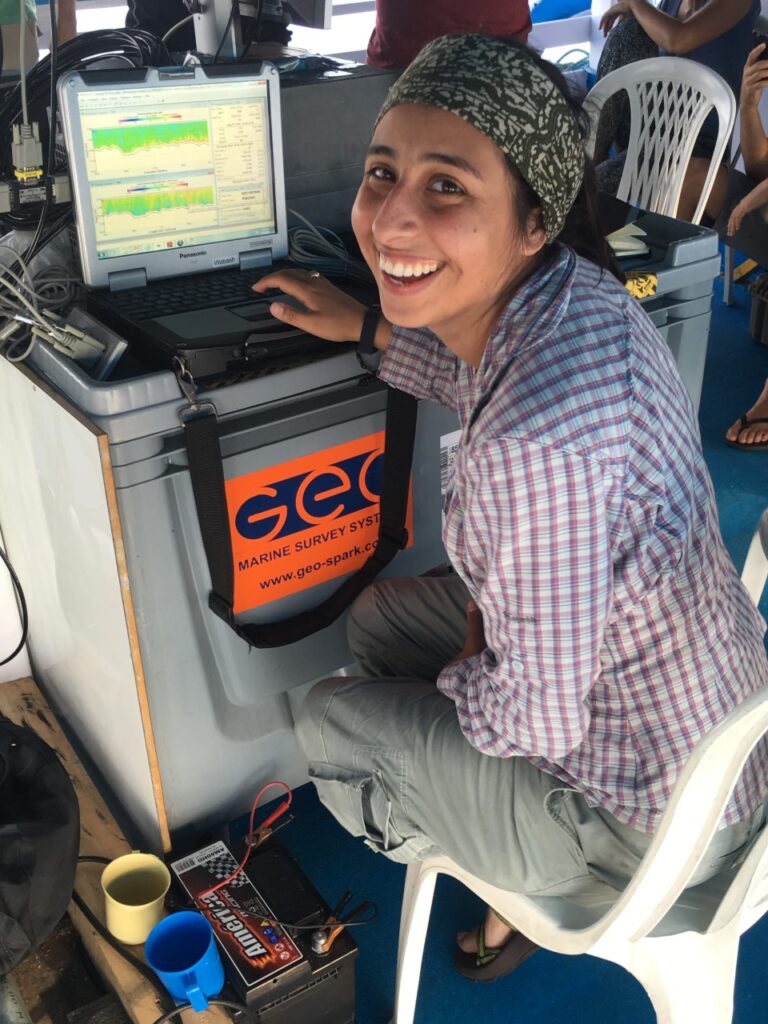 Julia smiling at the camera while working at a data terminal on a research vessel