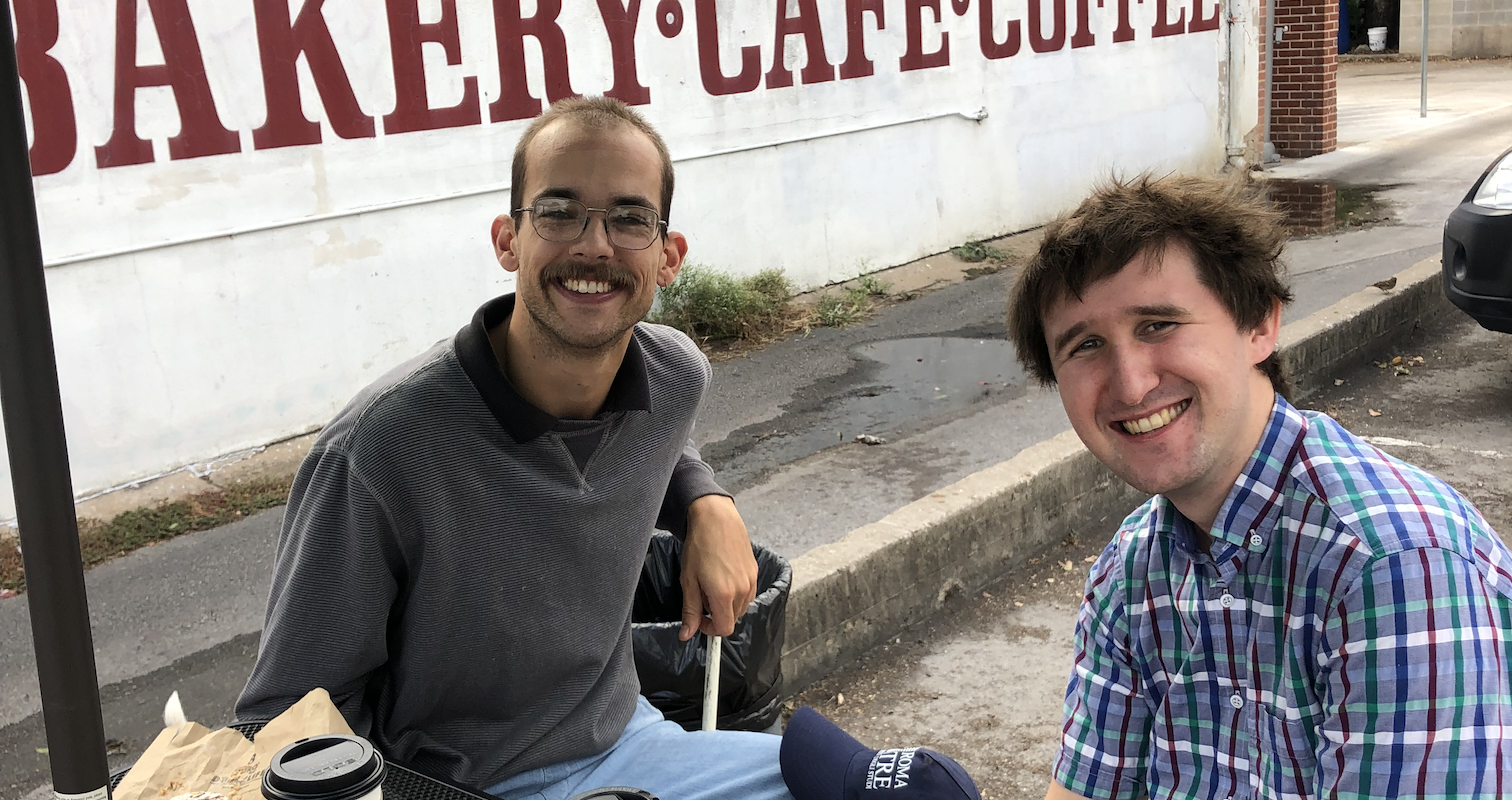 Ethan and Edward sitting at a table outside the cafe smiling at the camera.