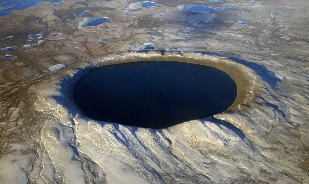 Aerial photo of the crater lake. The light colored sides contrast against the dark water of the lake.