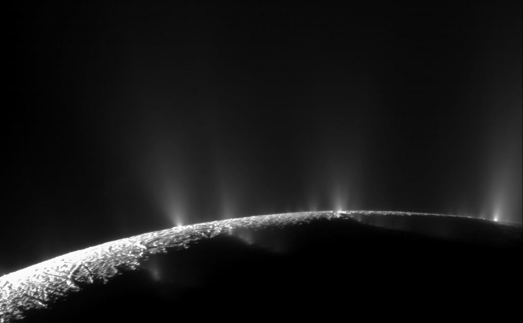 A black and white photo of Enceladus's icy surface showing several plumes spraying mist-like material into space.