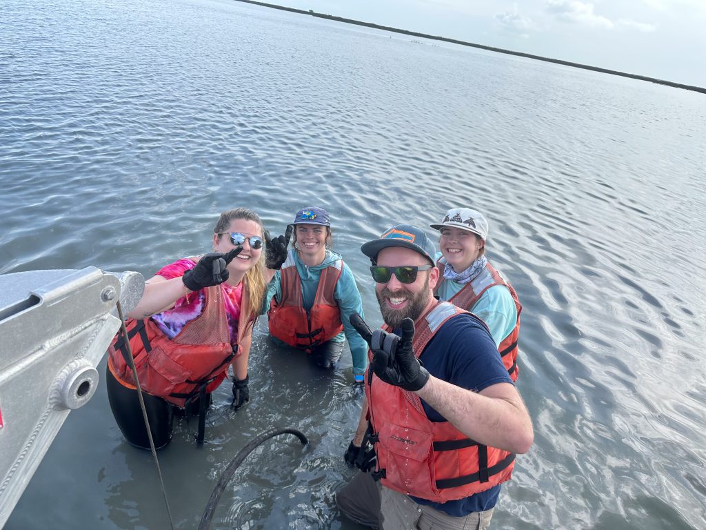 Photo of four people flashing a hook'em at the camera while waist high in water