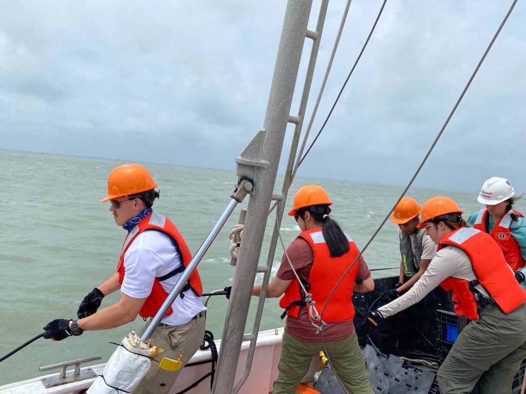 Students on a boat wearing hardhats and pulling together on a rope.