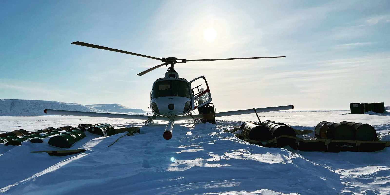 Photo of a helicopter on an icy landscape with the sun behind it.