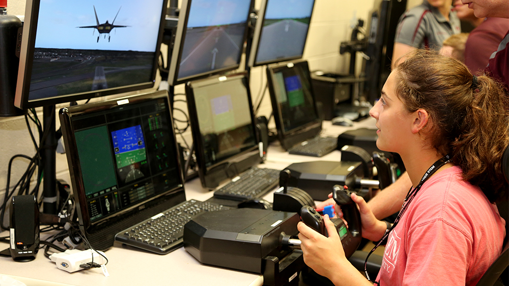 Photo of a student at a console holding a flight control and piloting a jet on screen.