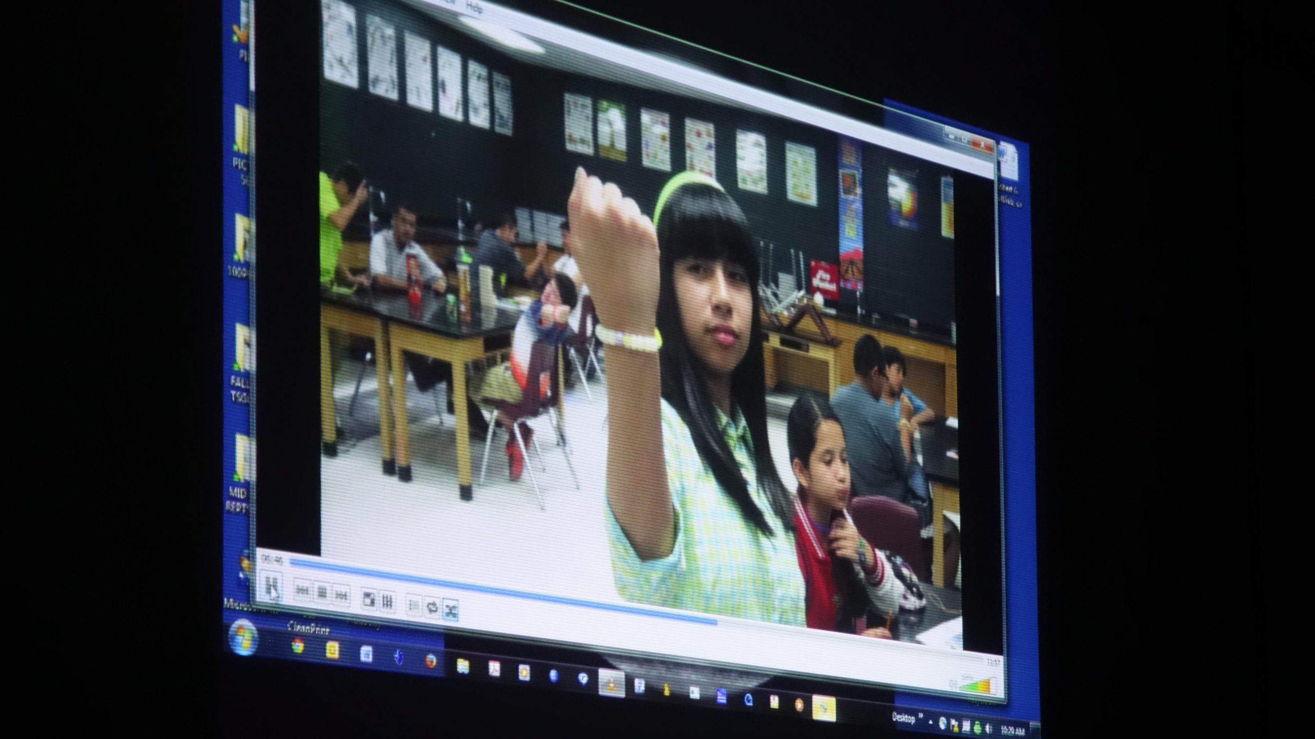 Photo of a TV screen showing a girl holding up her arm around her wrist is a high tec bracelet.