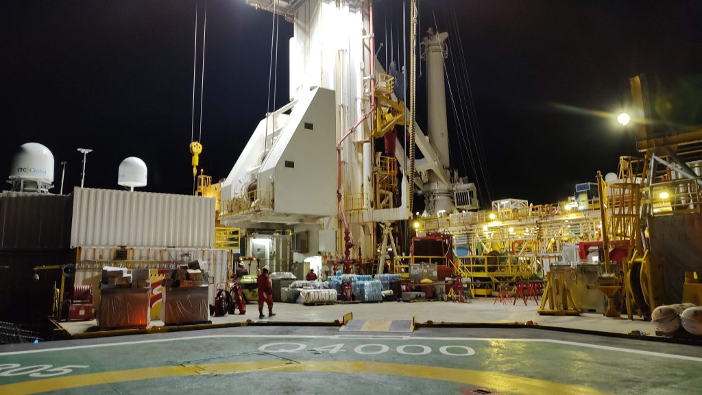 The rig floor lit up at night. Workers are visible in the center of the photo.