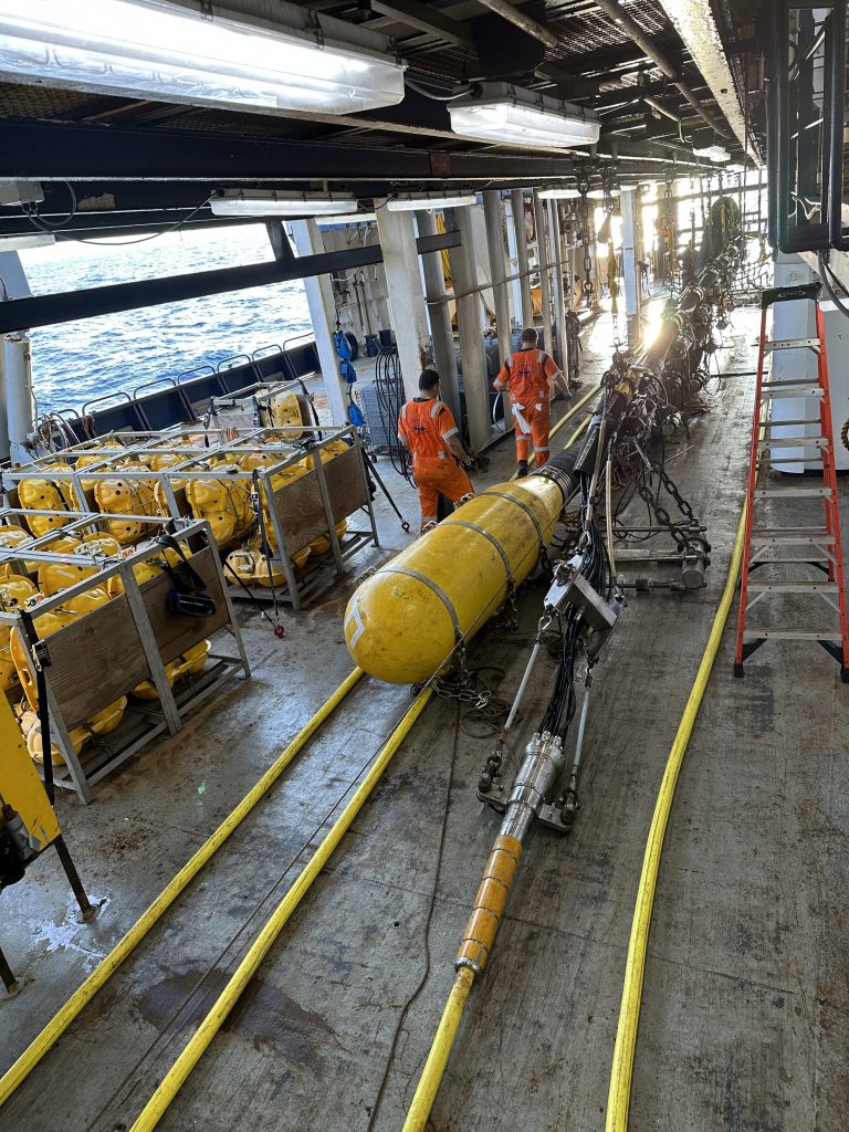 Large, yellow equipment is being worked on below deck. The sea is visible.