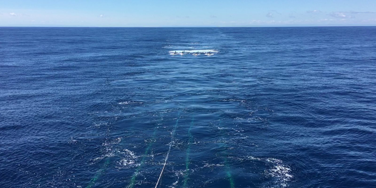 A photo of the ocean showing several underwater cables just under the surface, leading to the airgun towed some distance away.