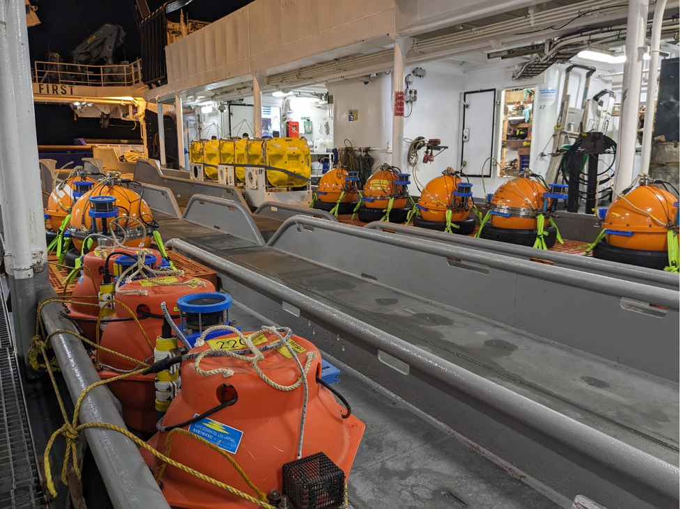 Photo of brightly colored buoys (or ocean floor seismometers) lined up on a ship's deck.