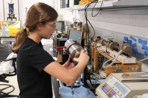 Photo of Caroline Seyler working on an apparatus in the lab.