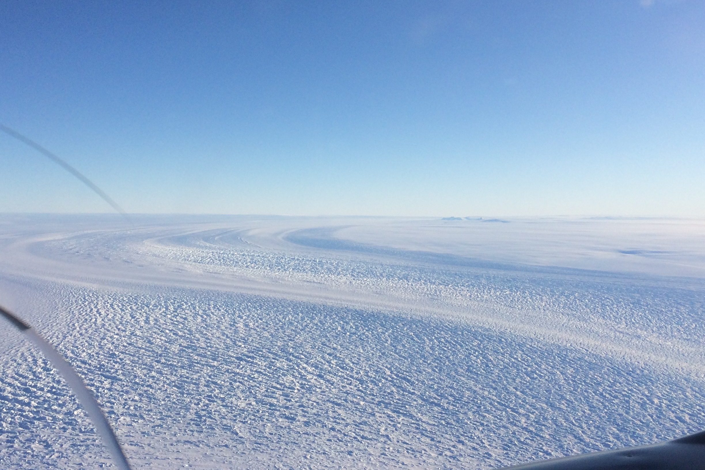 Photo of an ice sheet from high altitude. The ice extends unbroken to the horizon. 