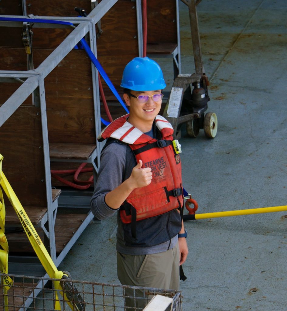 Photo of Jingxuan wearing life vest and hardhat on the deck of a research vessel.
