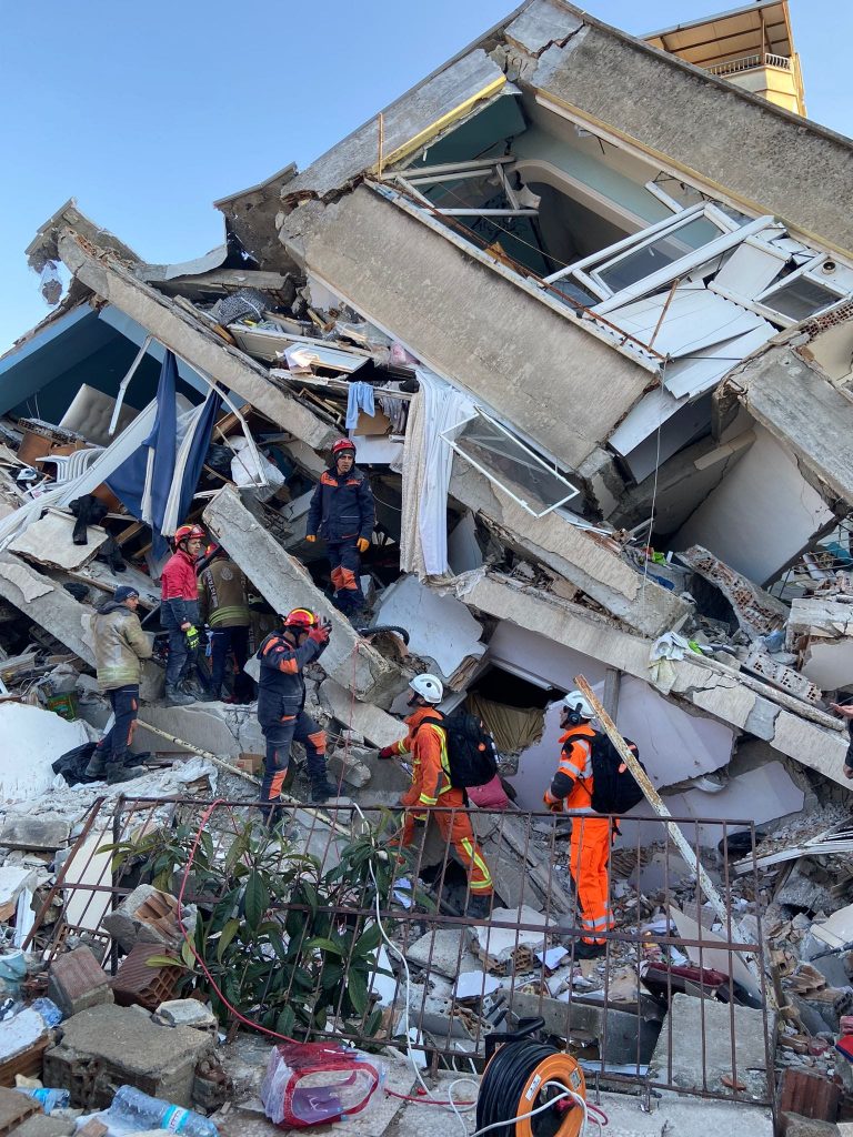 Photo of rescue workers in safety gear picking through a ruined building.