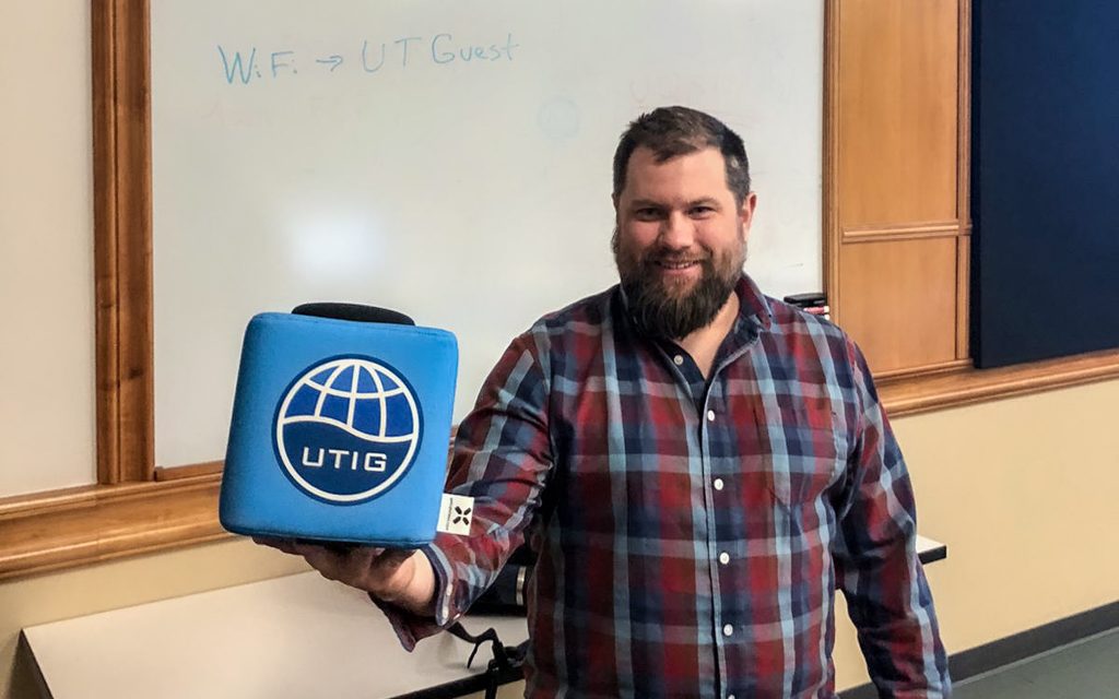 Photo of Luke Zoet holding the UTIG cube in the seminar room.