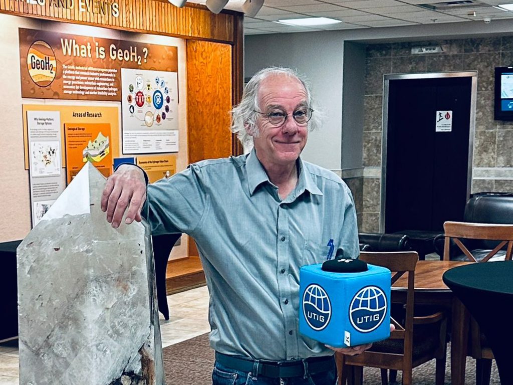 Photo of Steven holding the UTIG cube in the BEG lobby near a crystal.