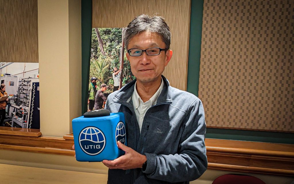 Photo of Shuichi Kodaira holding the UTIG cube in the seminar room.