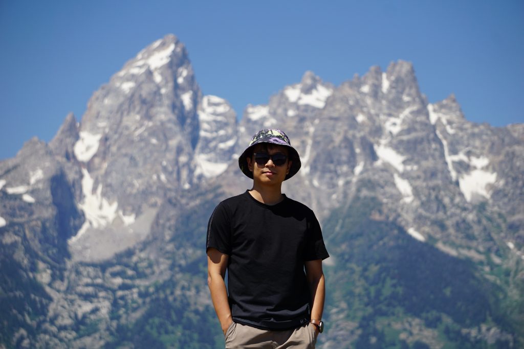 Photo of Enze wearing a hat sunglasses looking pretty chill in front of some spectacular mountains.