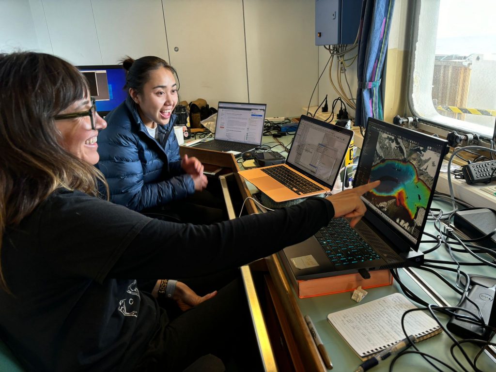 Photo of the scientist looking excitedly at and pointing at a laptop screen showing mission science.