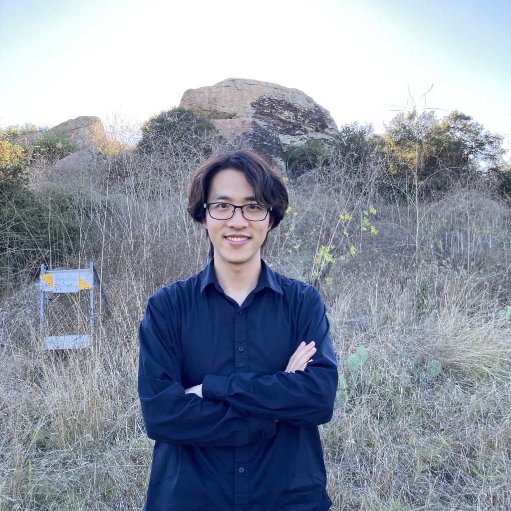 Photo of Zhe with arms crossed in a field.