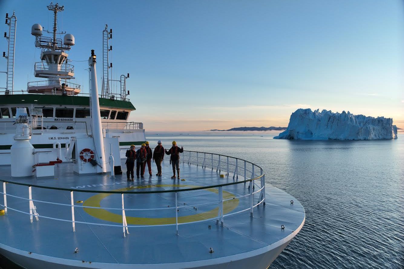 Aerial photo of ship with an ice berg in the background.