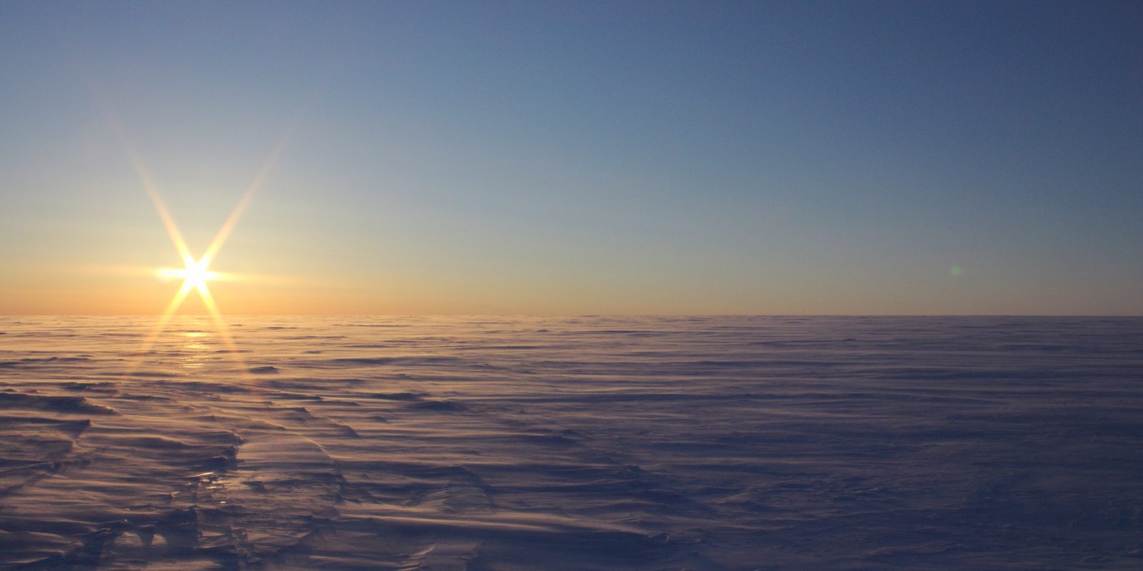 The sun low on the horizon over an icy landscape.