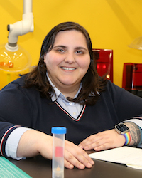 Portrait photo of Sara sitting at a table in a yellow lab.