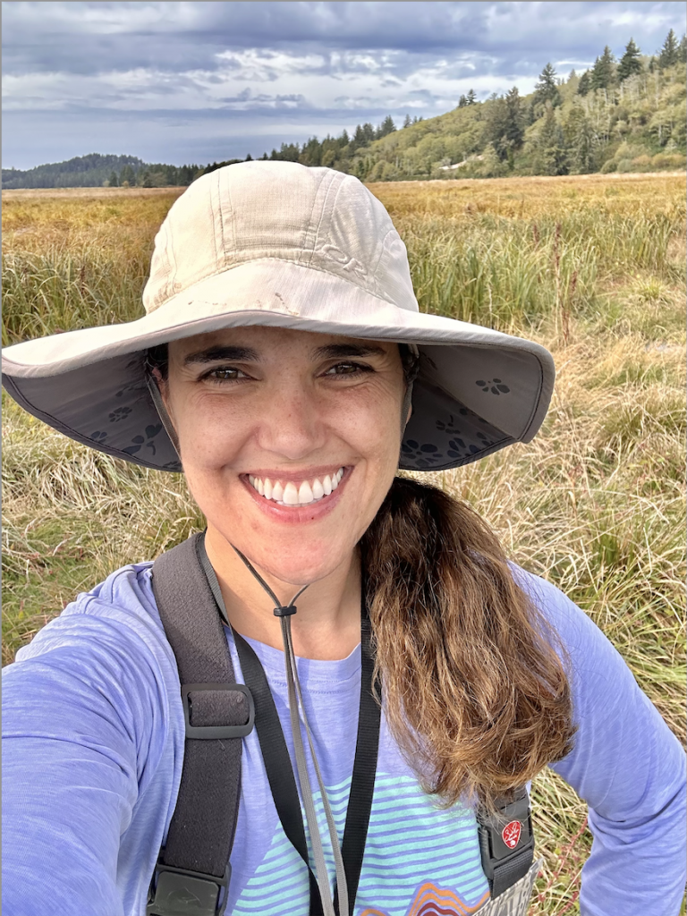 A picture of Tina wearing a hat in front of an empty grass field.