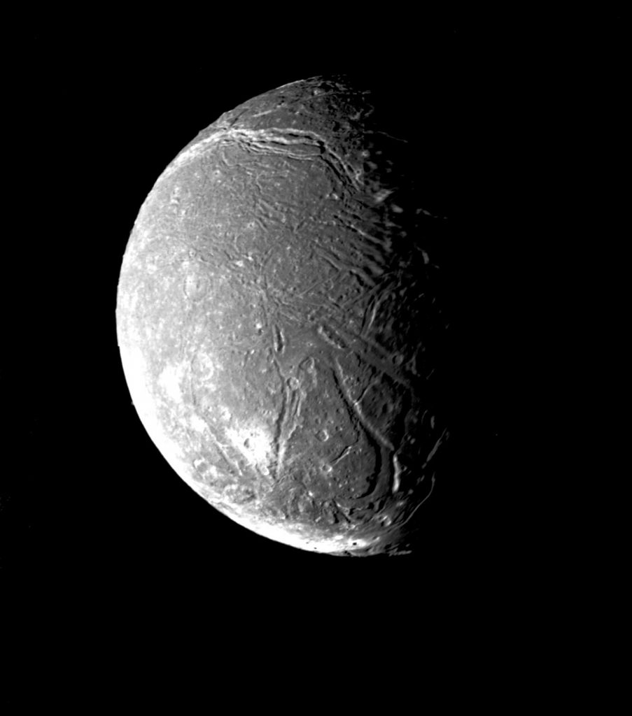 An image of Ariel from space. About a third of the moon is in shadow. The surface is pocked and ridged with several bright white regions.