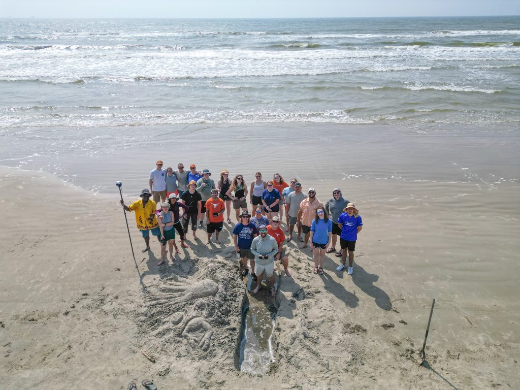 Aerial photo of a group of people on the beach with the sea behind them.