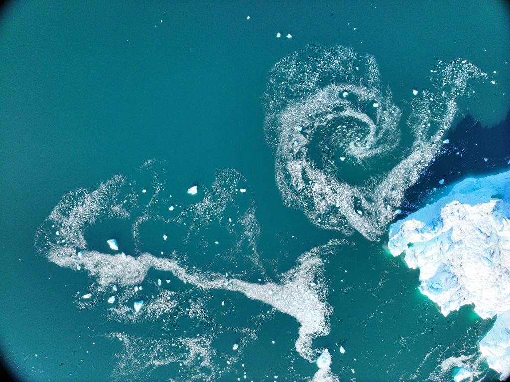 Top down view of a swirling muddy plumes at the edge of the ice.