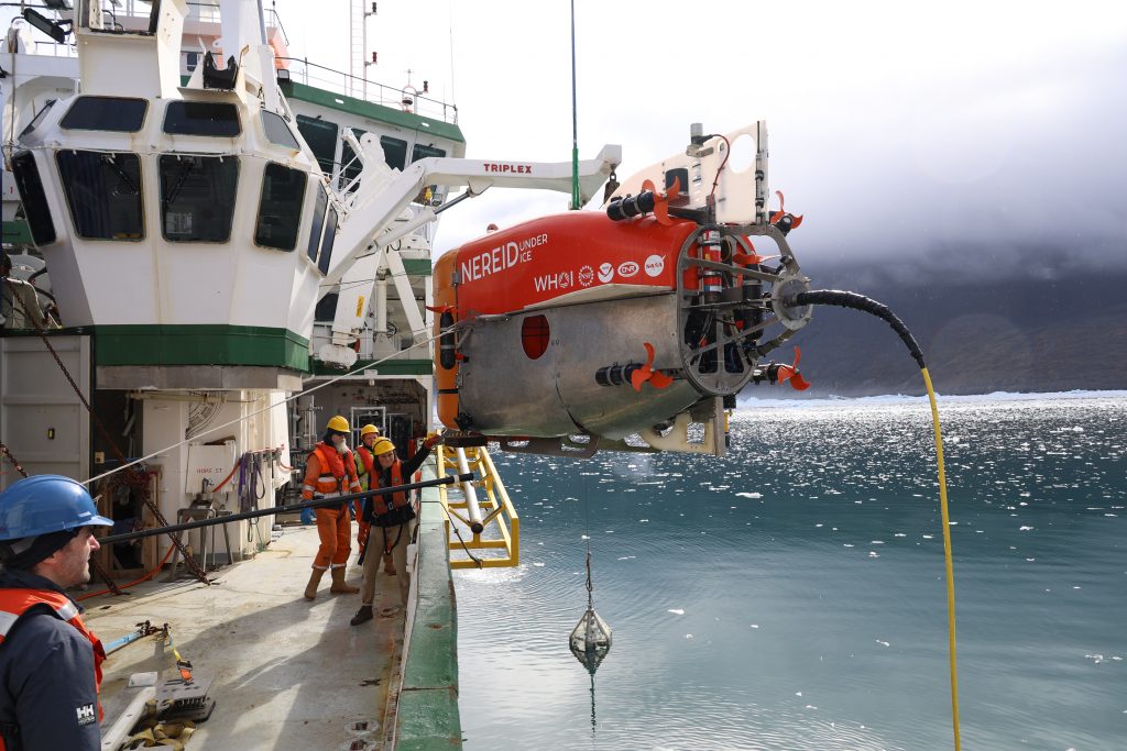 Photo of the submersible being lifted out of the water with a crane. Engineers are also on deck looking busy.