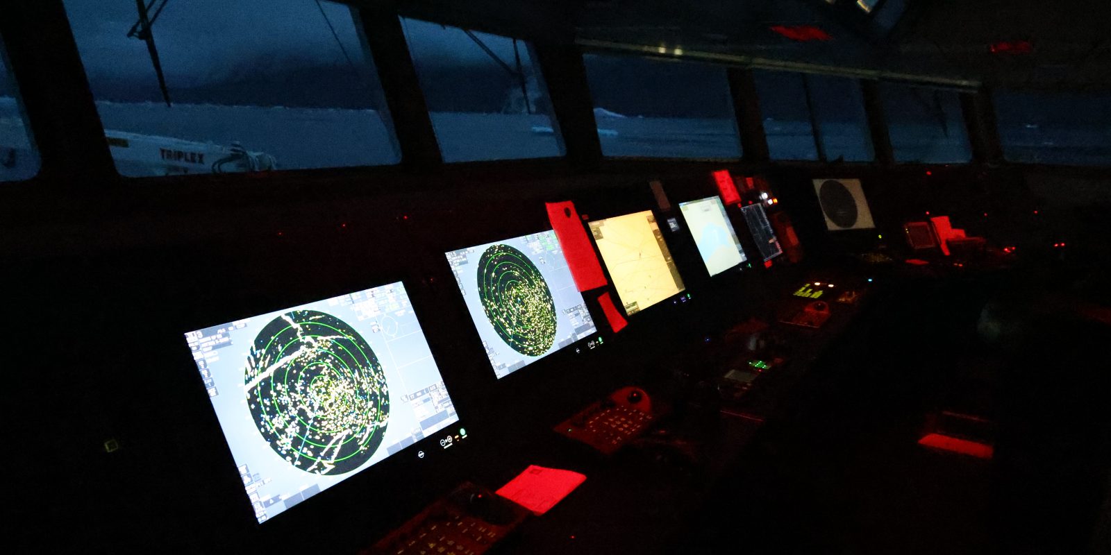 The darkened bridge by night. Screens glow under red lights.