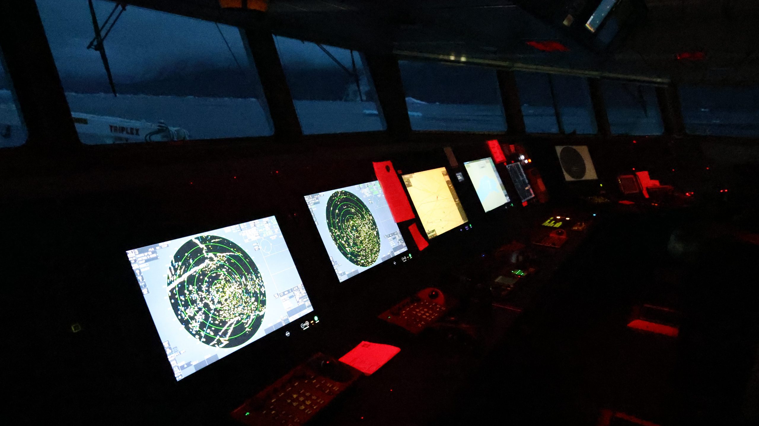 The darkened bridge by night. Screens glow under red lights.