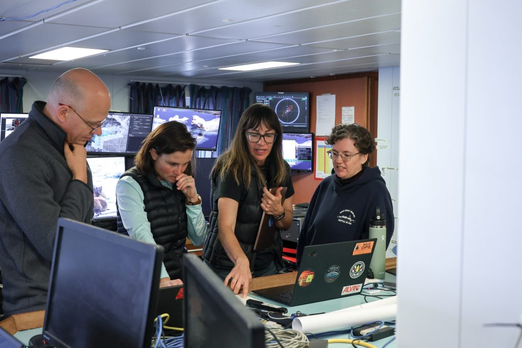 Photo of four of the the scientists looking over a laptop in the science operations room.